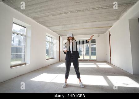 Il progettista della casa allunga la sua mano mentre si alza all'interno di una stanza e usando gli occhiali di realtà virtuale Foto Stock