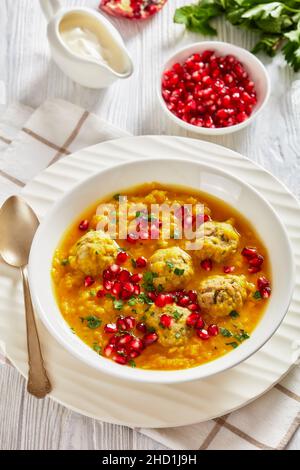 Ash-e Anar, zuppa di melagrana gialla in due pezzi iraniana con polpette di carne, zuppa spessa, in una ciotola bianca su un tavolo di legno bianco testurizzato con ingredienti e Foto Stock