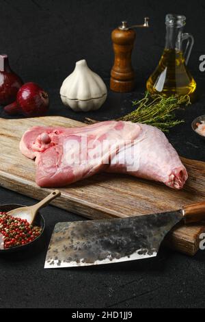 Gamba di tacchino crudo con la pelle sul tagliere con ingredienti da cucina su sfondo nero Foto Stock