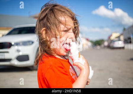 Ragazza caucasica con viso disordinato e mani che mangiano cono gelato Foto Stock