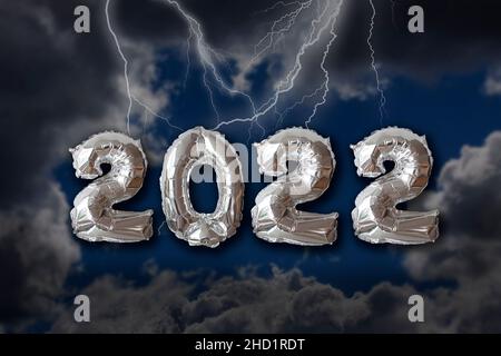 Anno 2022 scritto con i numeri di palloncino metallico d'argento con il cielo scuro drammatico, le nuvole e il fulmine. Concetto di cattive prospettive per l'anno. Foto Stock