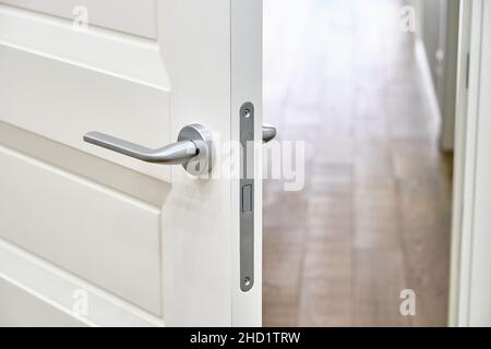 Elegante porta interna aperta bianca con maniglia in argento per la camera, elegante pavimento in parquet di quercia, vista ravvicinata degli interni contemporanei Foto Stock