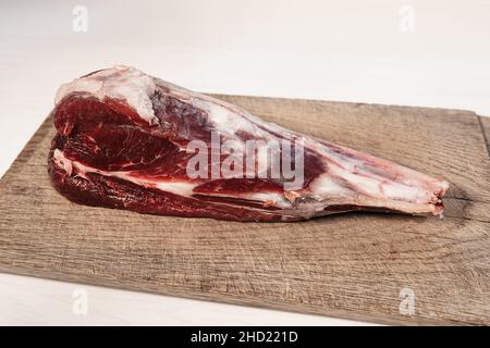 Stinco di agnello crudo fresco. Osso fresco di agnello crudo su tagliere di legno e bastone di pepe rosso caldo crudo Foto Stock