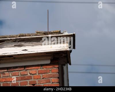 Angolo di una casa con un vecchio intemperie e rotto grondaia con tavole marciume e vernice peeling Foto Stock