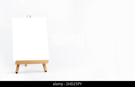 Cornice bianca su un piccolo cavalletto di legno su sfondo bianco con spazio per la copia. Pubblicità mockup tavola da disegno per immagini o grafica. Pittura fr Foto Stock