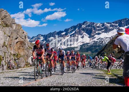 Un gran gruppo di ciclisti che corre sulla Tremola San Gottardo al Tour de Suisse 2021, circondando montagne innevate. Foto Stock