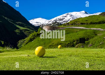 Un campo da golf, situato sulla strada del Passo Furka, montagne innevate intorno al Passo Furka in lontananza. Foto Stock