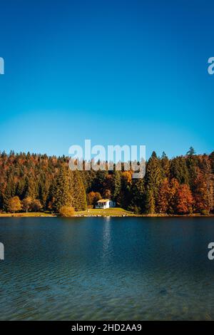 Magnifica vista di una casa solitaria sul lago panoramico e foresta autunno attraverso l'acqua Foto Stock