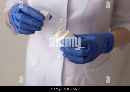 il medico sta aprendo un vaso di pillole a mano in guanti medici blu Foto Stock