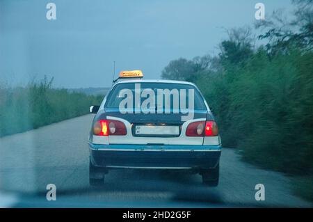 Vista posteriore di un taxi sulla strada in Congo al crepuscolo con palme. Ritorno a Pointe-Noire attraverso la vetrinetta. Foto Stock