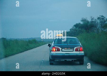 Vista posteriore di un taxi sulla strada in Congo al crepuscolo con palme. Ritorno a Pointe-Noire attraverso la vetrinetta. Foto Stock