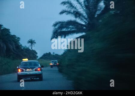Vista posteriore di due taxi sulla strada in Congo al crepuscolo con palme. Ritorno a Pointe-Noire. Foto Stock