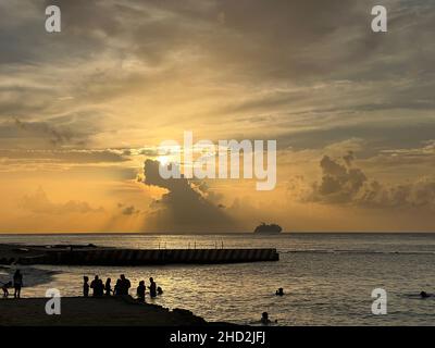 Silhouette di persone che guardano il tramonto a Cozumel, Messico. Grande nave da crociera che nuota sull'oceano durante il tramonto. Foto Stock