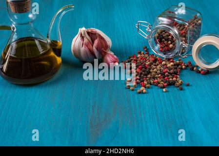 Sfondo di legno blu con una lattina d'olio, una testa di aglio e una pentola con pepe corns.Copy spazio. Foto Stock