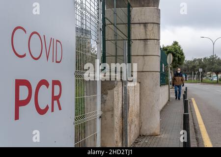 Primo piano di un poster della PCR Covid all'esterno di un centro di vaccinazione. Sullo sfondo, fuori fuoco, un uomo che indossa una maschera Foto Stock