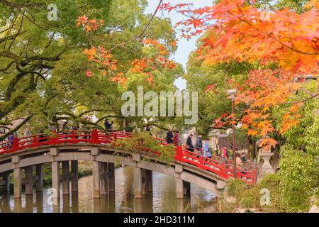tokyo, giappone - dicembre 07 2019: L'autunno giapponese momiji parte di fronte al ponte rosso Taiko Bashi del Santuario Shinto di Dazaifu attraversato da un gruppo Foto Stock