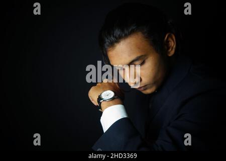 Primo piano di un uomo indiano che indossa un abito di classe e guarda su uno sfondo nero Foto Stock