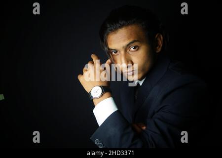 Primo piano di un uomo indiano che indossa un abito di classe e guarda su uno sfondo nero Foto Stock