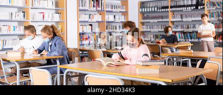 Adolescenti in maschere che trascorrono del tempo in biblioteca Foto Stock