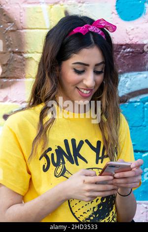 Street fashion ritratto di giovane donna guardando il suo smartphone nel quartiere della moda a est di Londra Shoreditch , Regno Unito Foto Stock