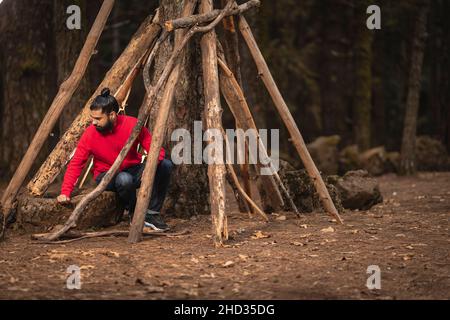 Fuoco poco profondo di un giovane ispanico con una barba seduta accanto ad un albero nella foresta Foto Stock