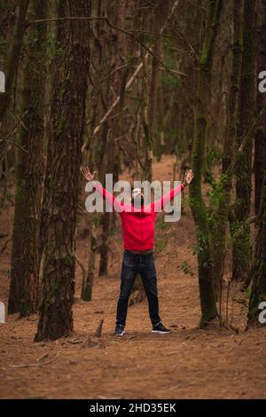 Colpo verticale di un uomo ispanico barbuto che sparge le braccia nella foresta Foto Stock