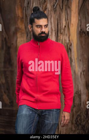 Colpo verticale di un uomo ispanico barbuto che indossa un maglione rosso nella foresta Foto Stock