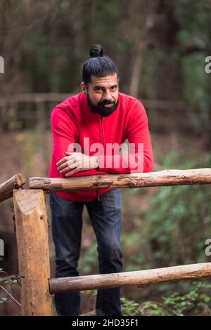 Colpo verticale di un giovane ispanico appoggiato su una recinzione nella foresta Foto Stock