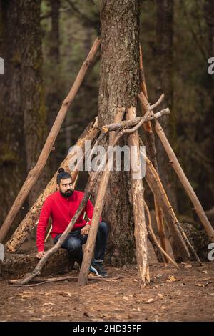 Colpo verticale di un uomo ispanico barbuto seduto accanto ad un albero nella foresta Foto Stock