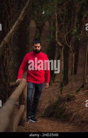 Colpo verticale di un uomo ispanico barbuto che indossa un maglione rosso nella foresta Foto Stock