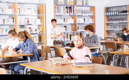 La studentessa di dieci anni in una maschera protettiva scrive un estratto da un libro di testo Foto Stock