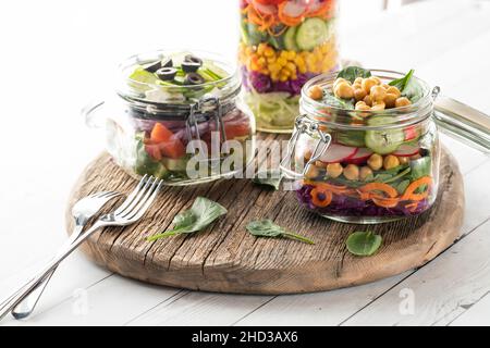 Vasetti di insalata freschi su un asse di legno luminoso da dietro. Foto Stock