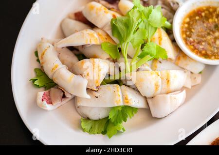 Calamari freschi alla griglia, primi piatti thailandesi grigliati calamari freschi in piatto bianco con salsa piccante e aspre o salsa di pesce, immagine vista dall'alto. Foto Stock