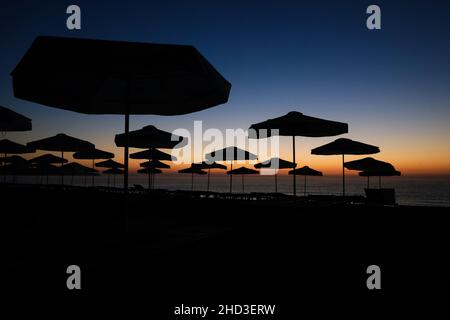 Sagome di ombrelloni sulla spiaggia poco prima dell'alba in una tranquilla e calda mattinata estiva al Mar Nero nel resort Obzor in Bulgaria. Foto Stock