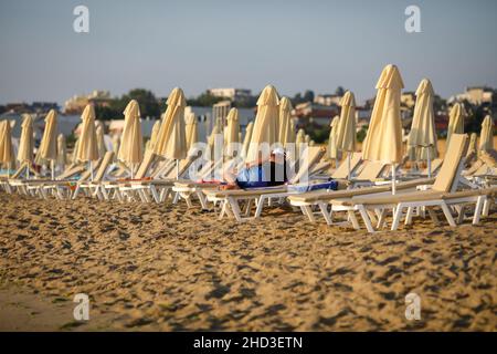 Uomo seduto su una poltrona sulla spiaggia in una tranquilla e calda mattinata estiva al Mar Nero nel resort Obzor in Bulgaria. Foto Stock