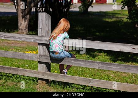 Umea, Norrland Svezia - 24 giugno 2020: La bambina con capelli rossi siede su una recinzione ed è annoiata Foto Stock