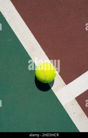 Palla da tennis gialla adagiata sulla linea del campo rosso e verde. Vista con disposizione piatta. Spazio per il testo Foto Stock