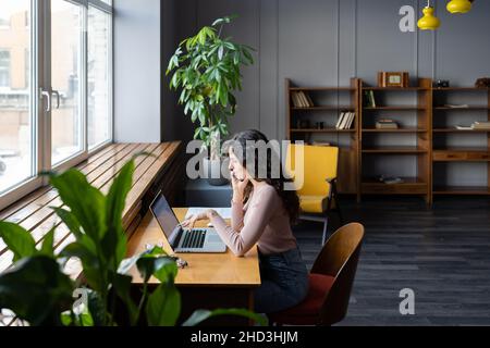 Donna d'affari che lavora sul laptop in uno spazio di coworking, che discute di rapporto finanziario via il telefono mobile Foto Stock