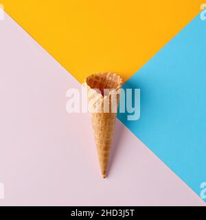 Un cono vuoto per gelato al wafer su sfondo colorato rosa giallo blu. Vista superiore piana. Foto Stock