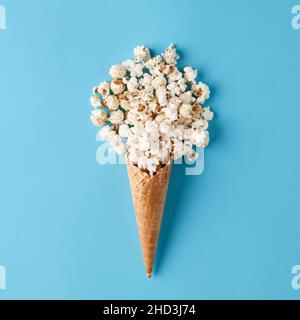 Cono gelato con popcorn versato su sfondo blu pastello. Concetto di cibo per la vita morta con una vista piatta. Foto Stock