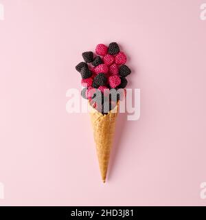 Cono gelato con lampone versato o bacche su sfondo rosa pastello. Concetto minimo di cibo per la vita morta creativa. Foto Stock