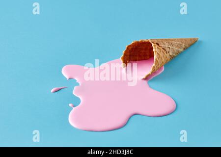 Gelato rosa che si scioglie e si spargerà dal cono di cialda su sfondo blu pastello. Concetto di cibo estivo minimalista. Foto Stock
