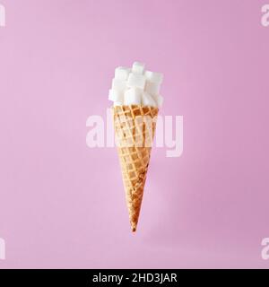 Cubetti di zucchero sul cono gelato su sfondo rosa. Minimalistica dipendenza da cibo dolce e dieta di zucchero per concetto di salute. Foto Stock