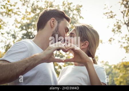 Giovani amanti baciare stand pronti a unire le mani per formare un cuore nel parco. Le coppie adolescenti si amano nel parco. Concetto di giovane coppia Foto Stock