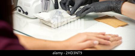 Mani in guanti neri di manicurista preparazione di speciale lima per unghie per trattamento manicure in un salone di bellezza Foto Stock