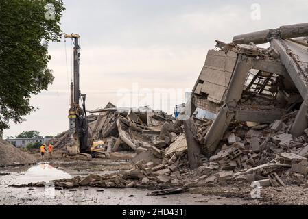 Perforare l'escavatore tra edifici in cemento collassato Foto Stock