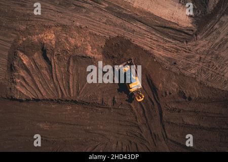 Il bulldozer cingolato giallo esegue lavori di terra - scatto con vista aerea. Il trattore cingolato giallo rastrema il terreno per costruire una strada asfaltata. Apripista terra lavora durante la costruzione della strada di percorso. Foto Stock