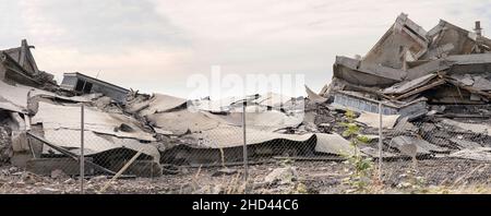 Calcestruzzo industriale distrutto da sciopero. Scenario di disastro pieno di detriti, polvere e edifici schiacciati. Foto Stock