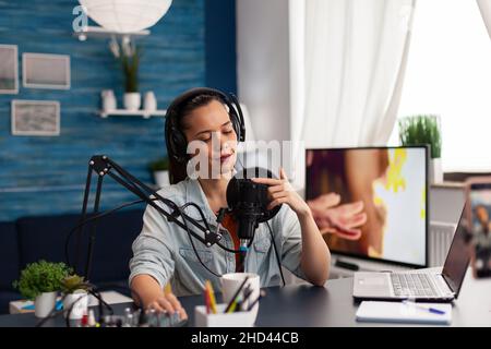 Creatore di contenuti toccare il microfono per testare l'audio. Vlogger che prova l'apparecchiatura audio con le dita. Donna influencer con cuffie in studio domestico che fa il controllo del suono per podcast online. Foto Stock