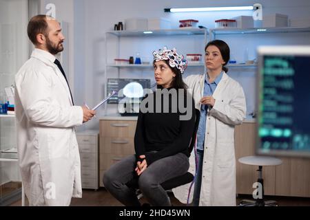 Medico di scienziato che discute i sintomi di malattia di neurologia con paziente di donna mentre ricercatore di neurologo che regola lo scanner di eeg durante l'esperimento di neuroscienza in laboratorio. Specialista che analizza l'attività cerebrale Foto Stock